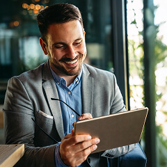 Hombre sonriendo y vistiendo traje social, sosteniendo y mirando una tablet.